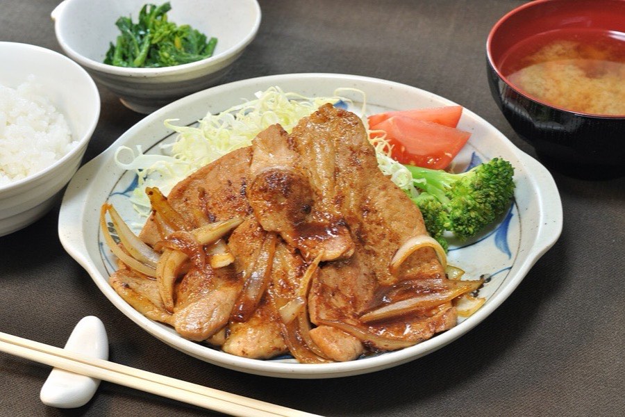 玉ねぎと焼いた豚の生姜焼きに千切りキャベツとトマトを添え、ご飯と味噌汁を並べた食卓