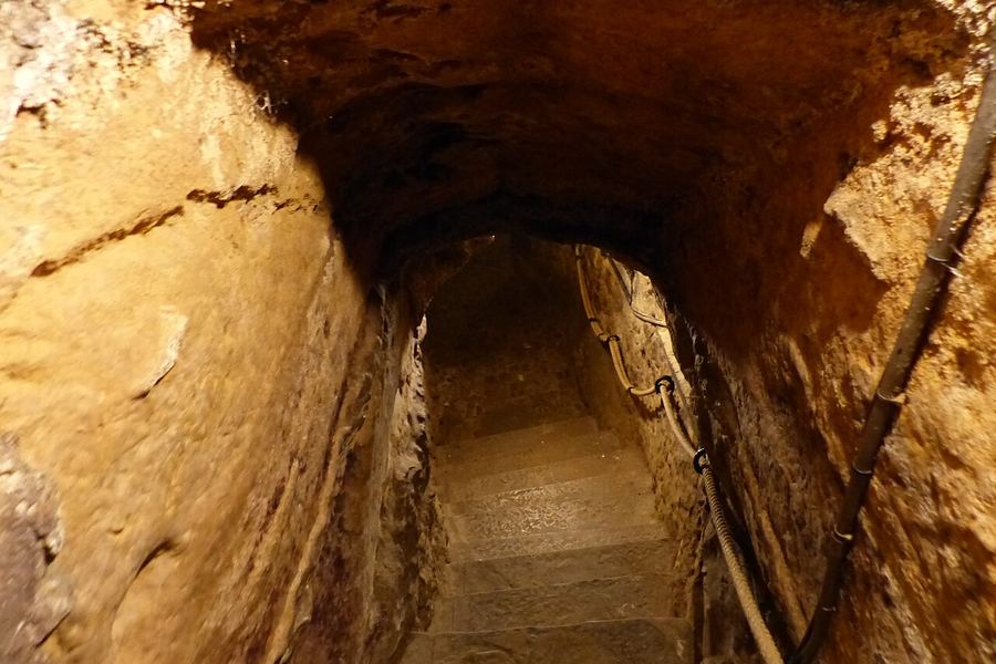 黄土色の岩をくり抜いた狭いトンネルが奥へ下っていき、壁の割れ目や削り跡が明かりに照らされている