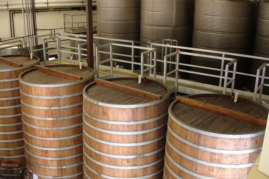 上部が開いた背の高い木製の大型発酵槽が並び、その奥に銀色のステンレスタンクが立ち並んでいる醸造所の内部