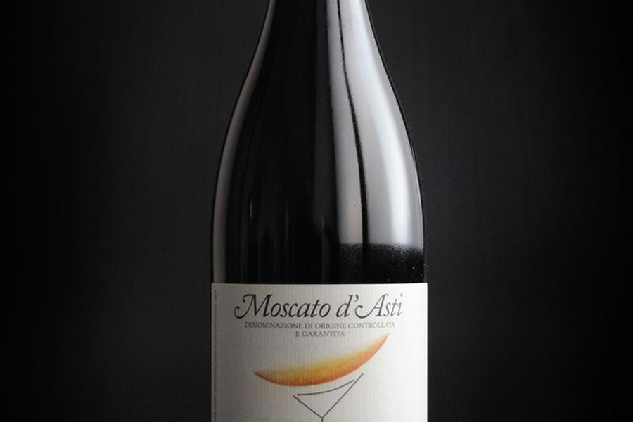 黒い背景に、Moscato d'Asti と書かれた白いラベルのボトルが一本立っている