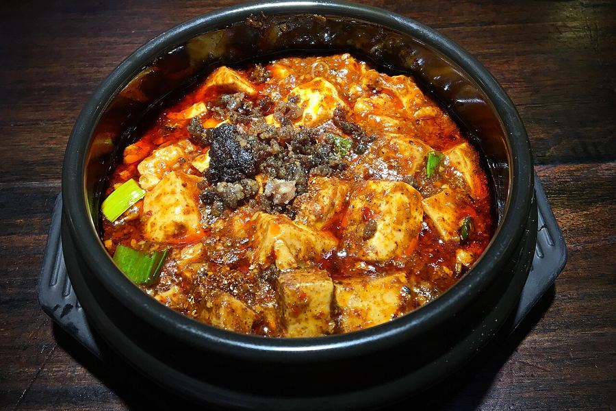 黒い土鍋に盛られた麻婆豆腐。赤いラー油の中に角切りの豆腐と挽き肉、青ねぎが見える