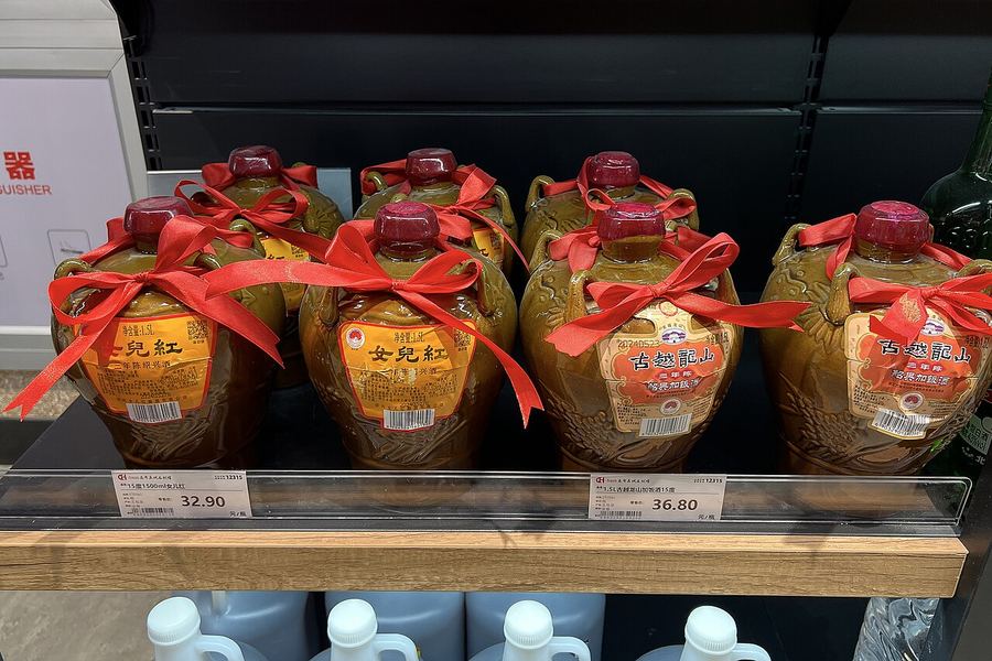 スーパーマーケットの棚に、赤いリボンを結んだ茶色の陶製の甕入り紹興酒がずらりと並んでいる