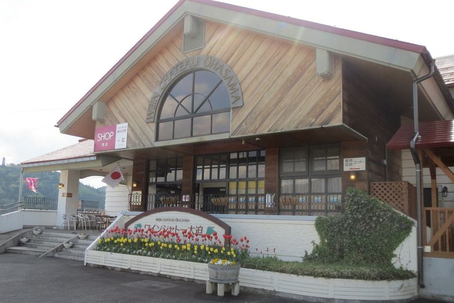 木の板張りの三角屋根に「WEIN CHATEAU OHASAMA」の文字。入口の前にはチューリップの花壇と「ワインシャトー大迫」の看板がある
