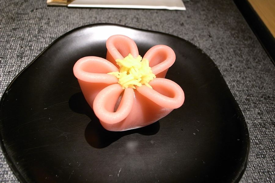 黒い漆の皿に、淡い紅色の花をかたどった上生菓子が一つのせられ、中心に黄色いそぼろがあしらわれている