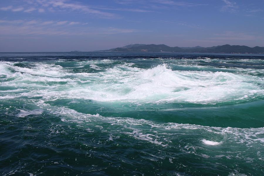 夕方の青い海に、白く泡立つ大きな渦潮がいくつも巻いている。水平線の奥には低い島影が見える