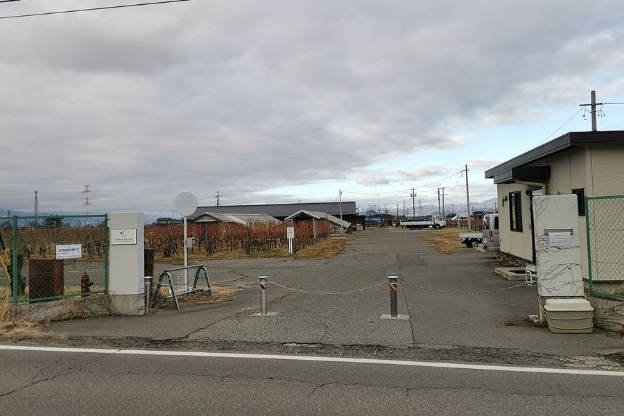 冬の曇り空の下、門柱の奥に葉を落としたぶどう棚と平屋の醸造棟が並ぶワイナリーの入口